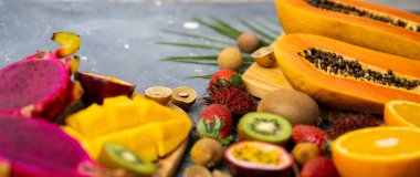 Gri mavi arka planda bir grup egzotik Thai meyvesi. Taze dilimlenmiş papaya, kivi, çarkıfelek meyvesi, Longan, ahşap kesim tahtalarında çilek. Metnin için alanı kopyala. Yaz, diyet, yemek. Düz yatıyordu.