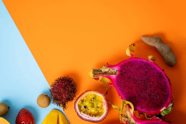 Summer tropical fruits composition. Horizontal shot of papaya, rambutan, mango, passion fruit, longan, strawberry isolated on pastel blue orange background with copy space. Top view.