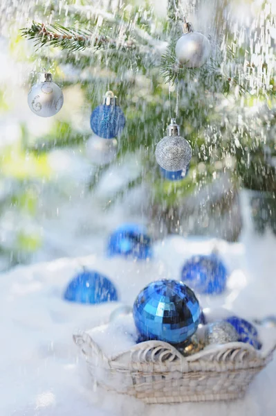 Vit korg med xmas bollar på snö och blå bollar på julgran — Stockfoto