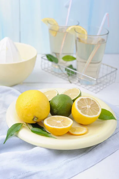 Bowl with fresh lime and lemon and two glass of lemonade on white wooden background