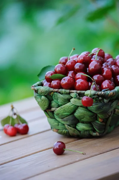 Cerejas maduras suculentas em uma cesta na mesa de madeira ao ar livre — Fotografia de Stock
