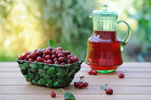 Jug of juice and basket with ripe cherries on wooden table outdoor — Stock Photo, Image