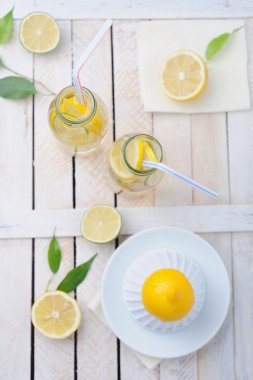 Fresh lime and lemon, squeezer and two glasses of lemonade on rustic table clipart