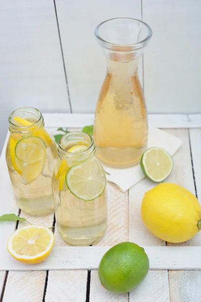 Kancsó és pohár limonádé, citrom és lime, a rusztikus asztal — Stock Fotó