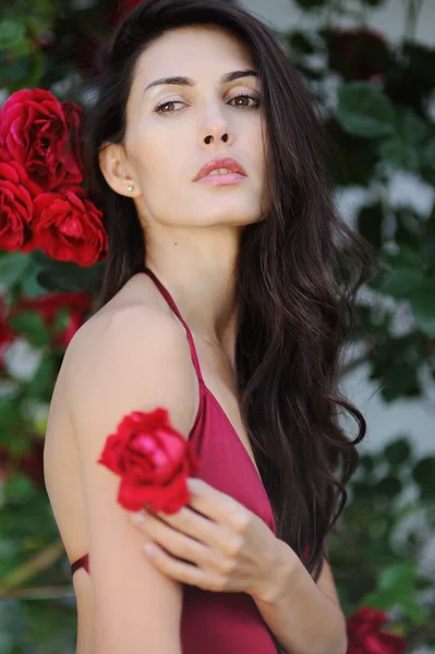 Portrait of beautiful brunette girl in red roses — Stock Photo, Image