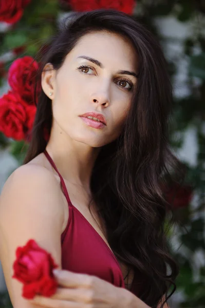 Portrait of beautiful brunette girl in red roses — Stock Photo, Image