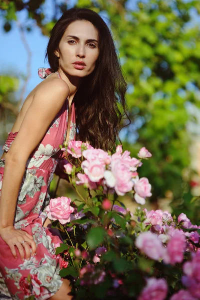 Jolie jeune femme au buisson de roses rouges dans la roseraie — Photo