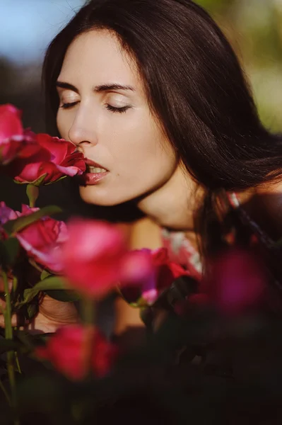 Schönes Mädchen, das eine Rose im Garten riecht — Stockfoto