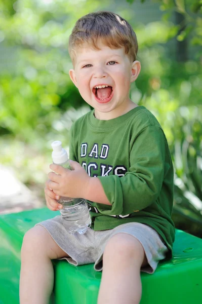 Attraktiver kleiner Junge trinkt Wasser aus Flasche im Freien — Stockfoto