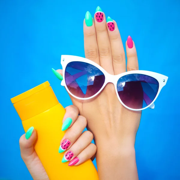 Mujer con uñas de gel sosteniendo gafas de sol y loción protector solar — Foto de Stock