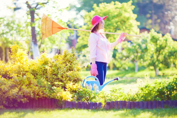 Mujer joven sosteniendo rastrillos en el jardín —  Fotos de Stock