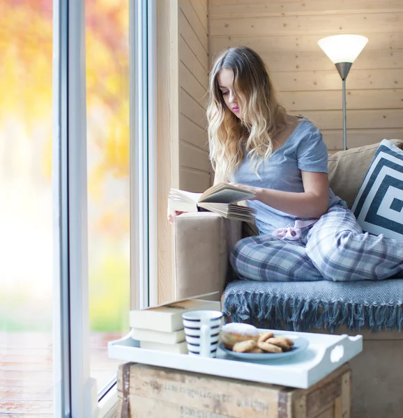 Jeune belle femme blonde avec une tasse de café assis à la maison par la fenêtre — Photo