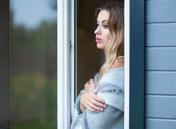 Jeune belle femme blonde debout à la maison par la fenêtre — Photo