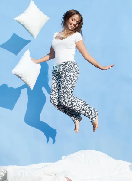 Γυναίκα που κρατά ένα μαξιλάρι πηδάω επάνω σε κρεβάτι — Φωτογραφία Αρχείου