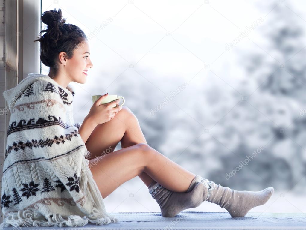 Woman drinking cup of coffee sitting by the window