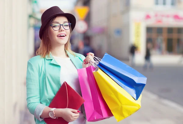 Jovem mulher comprador atraente usando chapéu e óculos segurando sacos de compras — Fotografia de Stock