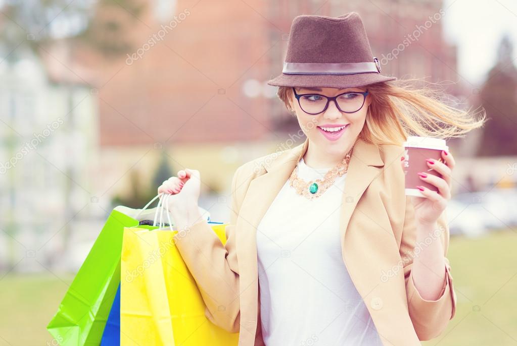 Young attractive shopper woman wearing hat and glasses holding shopping bags