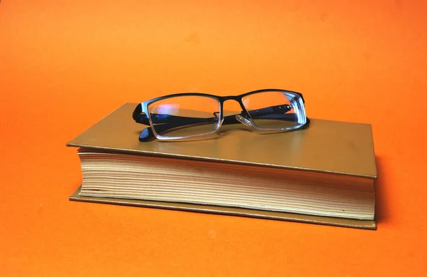 Gafas Sobre Libro Sobre Fondo Naranja —  Fotos de Stock