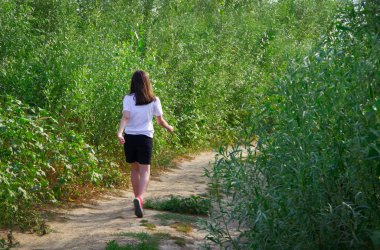 Kız sık ağaçların arasında bir orman yolunda yürüyor..