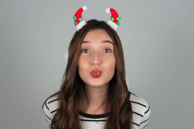 Genç bir kadın kameraya hava öpücüğü yolluyor. Saçında Noel süsleri olan bir kadın. Gri arka plan. Yüksek kalite fotoğraf