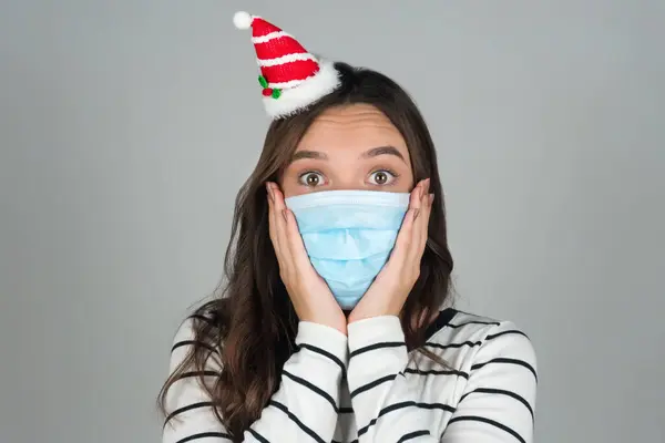 Una giovane donna con una maschera medica con una decorazione natalizia in testa. Festeggiare il Natale in una pandemia. — Foto Stock