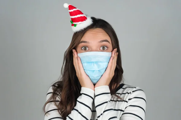 Kafasında Noel süsü olan tıbbi maskeli genç bir kadın. Noel 'i bir salgınla kutluyoruz. 