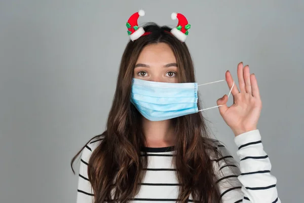 Una giovane donna con decorazioni natalizie nei capelli indossa una maschera medica. — Foto Stock