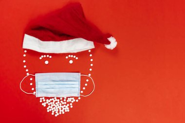 Beyaz yuvarlak tabletlerle kaplı Noel Baba heykelciği. Yüz maskesi, kırmızı arka plan. Yüksek kalite fotoğraf