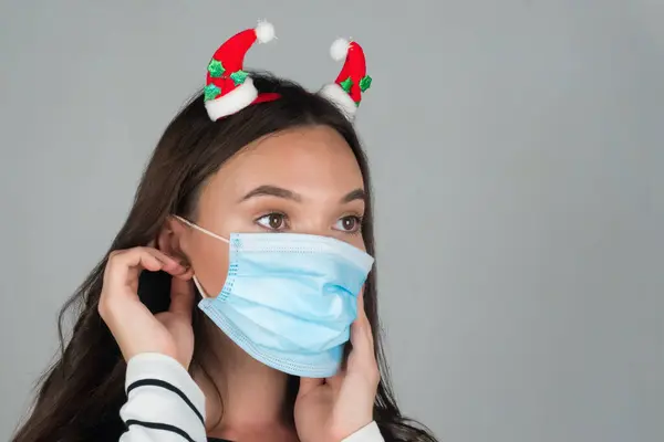 Una giovane donna con decorazioni natalizie nei capelli indossa una maschera medica. — Foto Stock