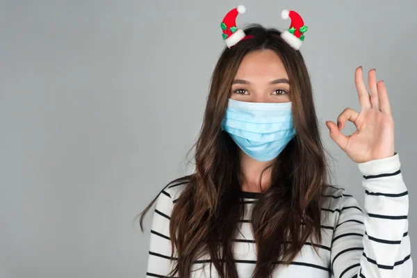 Yılbaşı için tıbbi maske takan genç bir kadın iyi bir jest gösteriyor. Noel 'i bir salgının ortasında kutluyoruz.