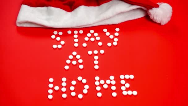 Kırmızı arka planda yuvarlak beyaz hapların harflerini yazmak için evde kal. Noel Baba şapkası — Stok video