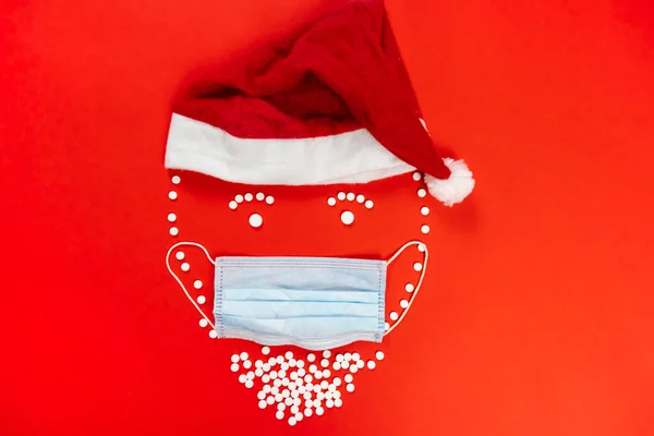 Beyaz yuvarlak tabletlerle kaplı Noel Baba heykelciği. Yüz maskesi, kırmızı arka plan. Yüksek kalite fotoğraf