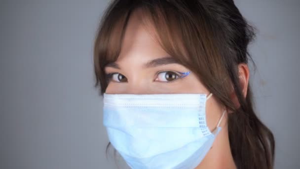 Jonge mooie vrouw met make-up en in een medisch masker kijkt naar de camera — Stockvideo