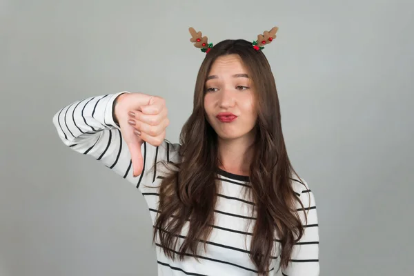 Dissatisfied woman shows a sign of approval, holds her thumb down, expresses dislike. Woman with Christmas decorations in her hair. High quality photo