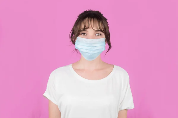 Genç bir kadın COVID-19 'dan korunmak için maske takıyor. Pembe arka planda izole edilmiş. Yüksek kalite fotoğraf