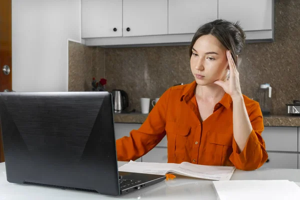 A woman leads a video conference while sitting at home in the kitchen. Work at home concept.