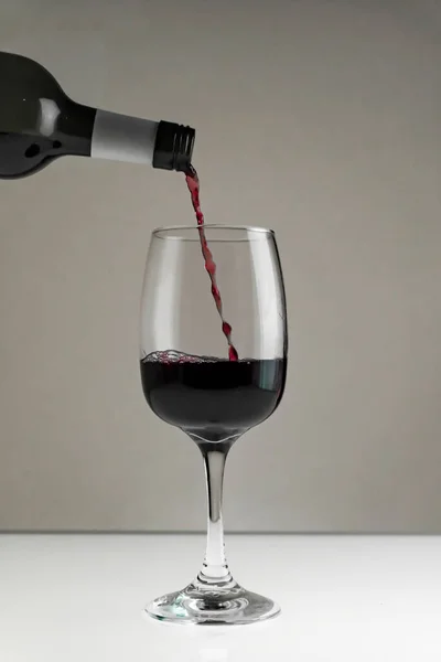 Red wine is poured from a bottle into a glass on a blurred background, close-up.