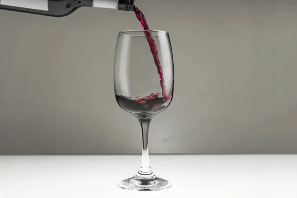Vinho tinto é derramado de uma garrafa em um copo em um fundo borrado, close-up. — Fotografia de Stock