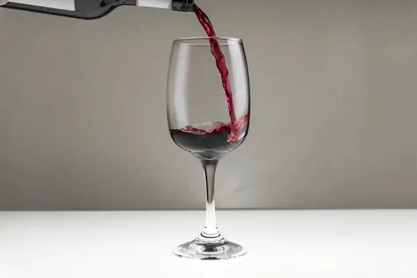 Vinho tinto é derramado de uma garrafa em um copo em um fundo borrado, close-up. — Fotografia de Stock