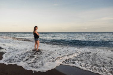 Genç bir kadın gün batımında deniz kıyısında yürüyor..