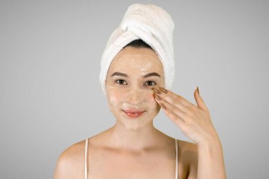 Kafasında banyo havlusu olan mutlu genç bir kadın temizlik köpüğü sürüyor..