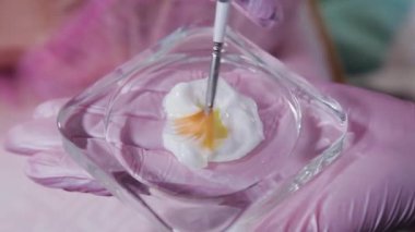 Kadın güzellik uzmanı fırçayla krem karıştırıyor..