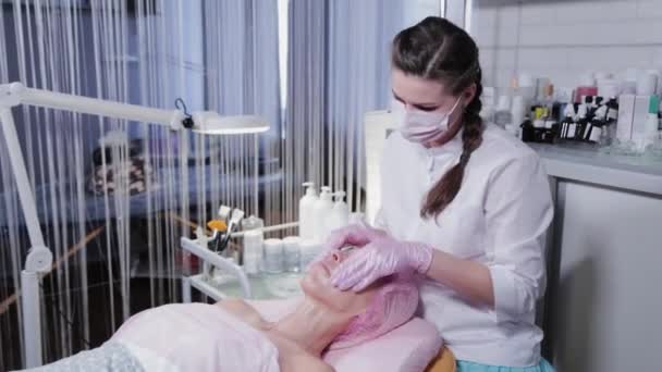 Жінка косметолог натирає крем на обличчі клієнта косметологічної клініки . — стокове відео