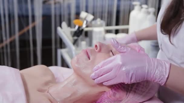 Женщина-косметолог натирает кремом лицо клиента косметологической клиники. — стоковое видео