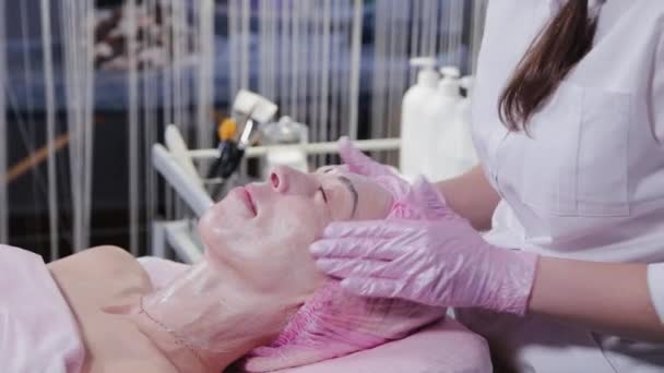 Mulher esteticista fazendo massagem facial para mulher jovem. — Vídeo de Stock