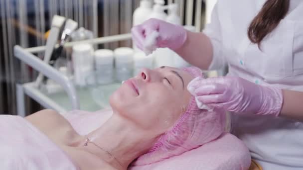 Kvinna kosmetolog raderar grädde från ansiktet på en ung kvinna. — Stockvideo