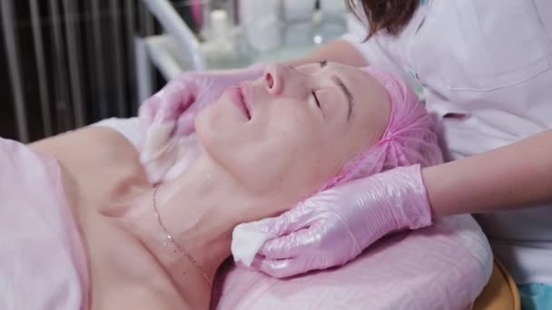 Női kozmetikus lemossa a krémet a fiatal nők arcáról. — Stock videók