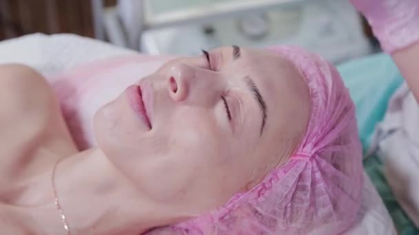 女性の美容師は女性患者の顔にクリームを塗る。フェイシャルマッサージ. — ストック動画
