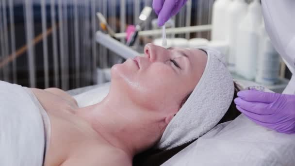 Vrouwelijke cosmetoloog past peeling toe op vrouwen van aangezicht tot cliënt van kosmetologische kliniek. — Stockvideo