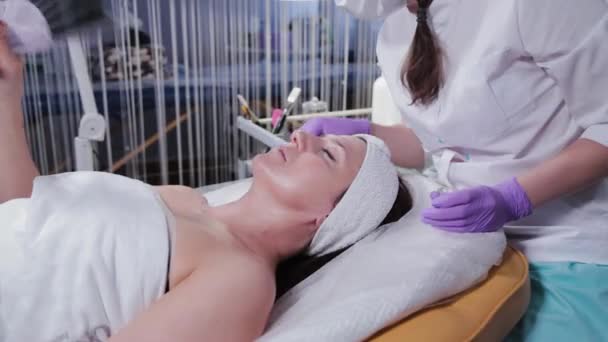 Kvinnlig kosmetolog applicerar peeling på kvinnor ansikte mot ansikte till klienten av cosmetology kliniken. — Stockvideo